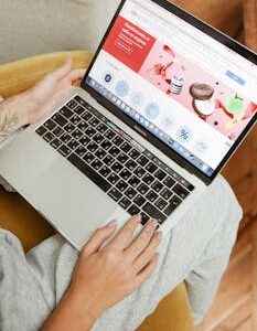 A woman sits comfortably indoors, browsing an online shopping website on her laptop.