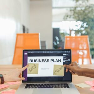 Hands pointing at business plan on laptop screen in modern office.